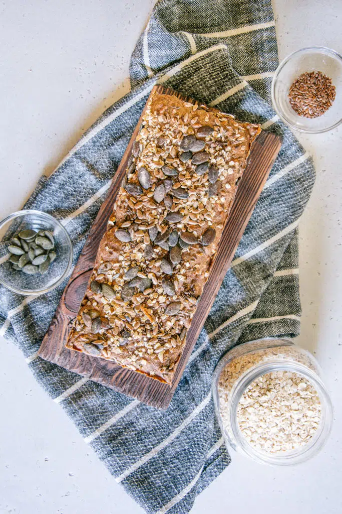 Vollkorn-Walnussbrot aus der Vogelperspektive diagonal im Bild ausgerichtet. Das Brot liegt auf einem Holzbrett, das auf einem gestreiften Küchentuch steht.