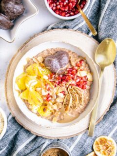 Lebkuchen-Porridge in einer weißen Schüssel auf einem runden Rindenbrett mit einem goldenen Löffel neben der Schüssel