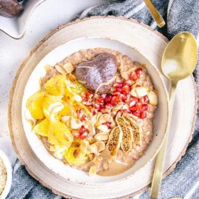 Lebkuchen-Porridge in einer weißen Schüssel auf einem runden Rindenbrett mit einem goldenen Löffel neben der Schüssel