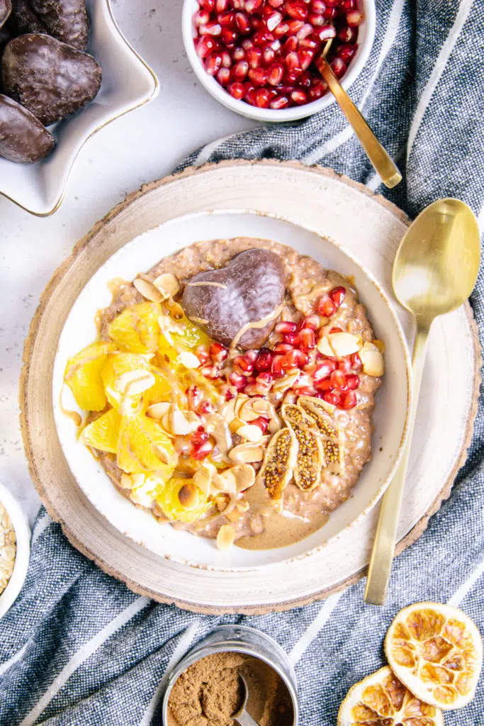 Lebkuchen-Porridge in einer weißen Schüssel auf einem runden Rindenbrett mit einem goldenen Löffel neben der Schüssel