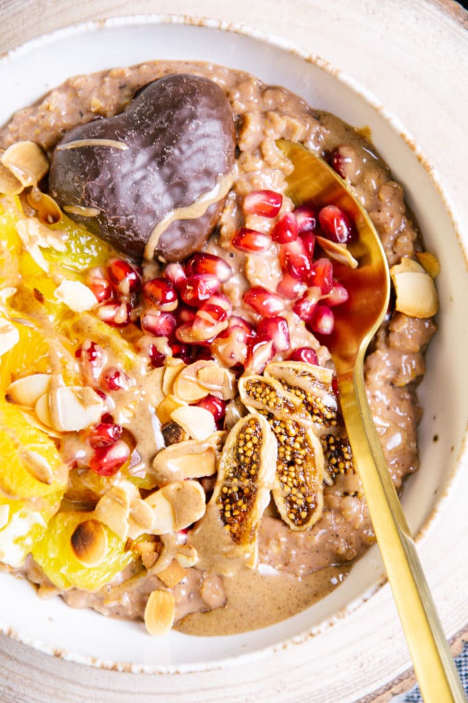 Nahaufnahme von oben von cremigem Lebkuchen-Porridge mit Früchten, Lebkuchenherz und Haselnussmus als Toppings
