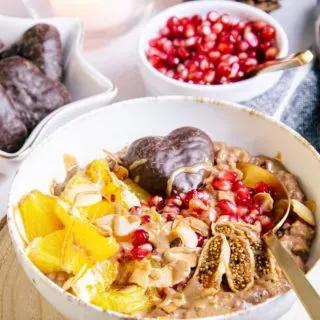 Lebkuchen-Porridge mit Orangenstücken, Granatapfelkernen, getrockneter Feige, Mandelblättchen und einem Lebkuchenherz als Topping. Aufnahme im 45-Grad-Winkel.