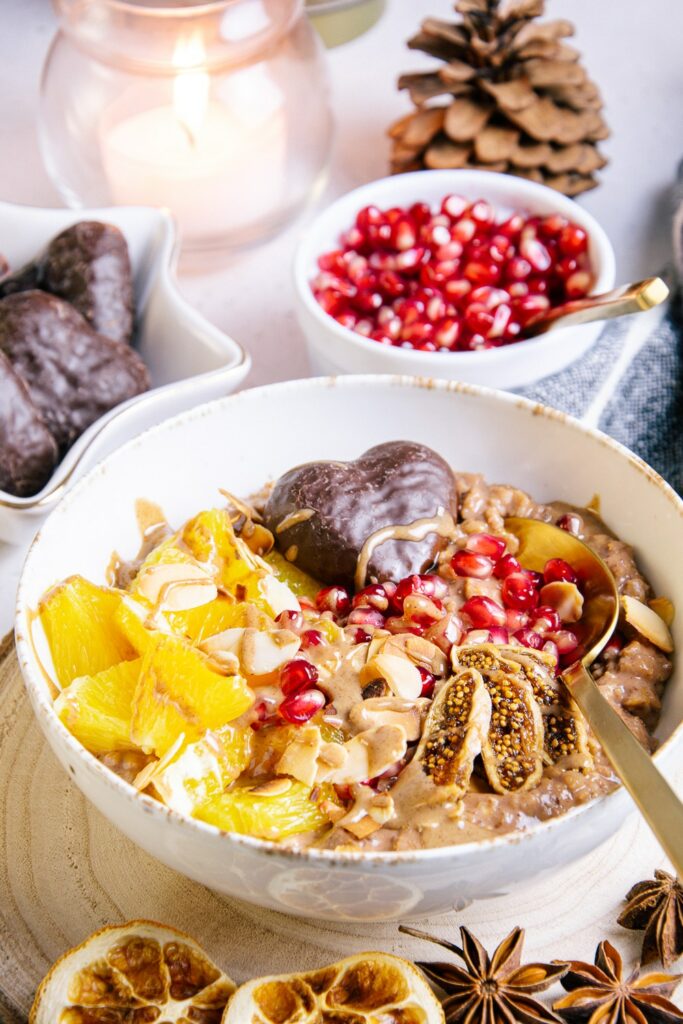 Lebkuchen-Porridge mit Orangenstücken, Granatapfelkernen, getrockneter Feige, Mandelblättchen und einem Lebkuchenherz als Topping. Aufnahme im 45-Grad-Winkel.