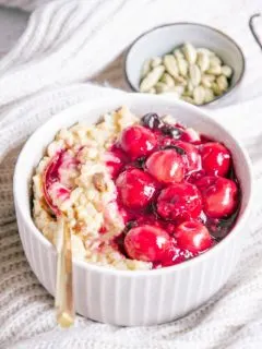 Veganer und zuckerfreier Milchreis mit Kirschkompott in einer grauen Schüssel mit goldenem Löffel im 45-Grad-Winkel fotografiert.