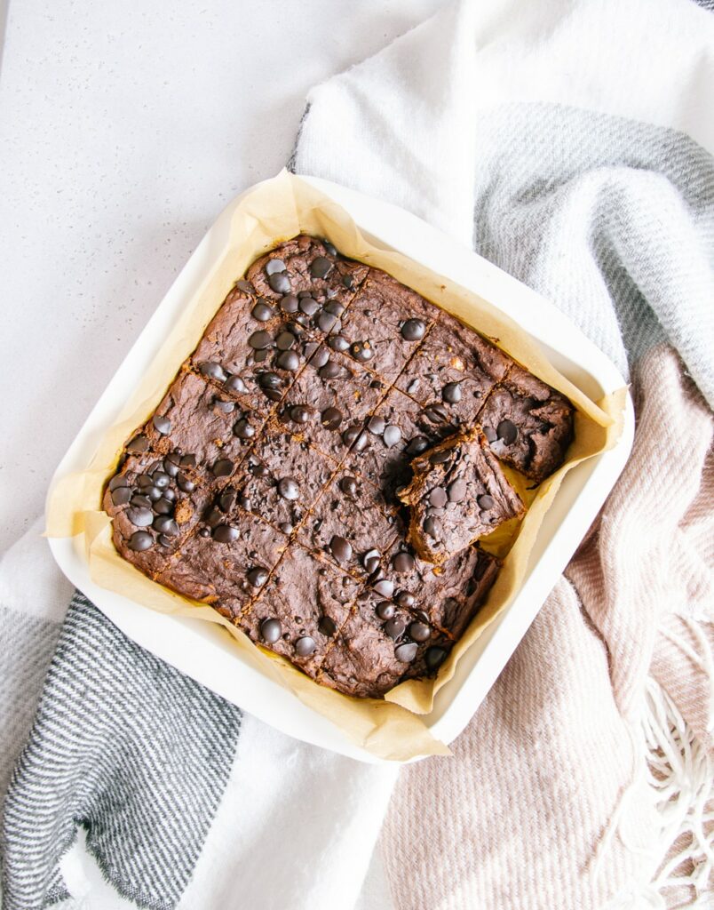 Vegane und zuckerfreie Protein-Brownies in der Backform von oben auf einer grau-braunen Decke fotografiert.