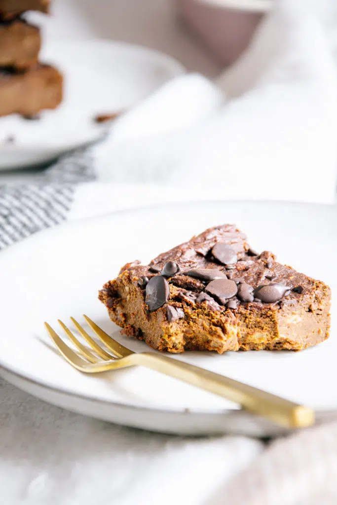 Veganer und zuckerfreier Protein-Brownie auf einem hellgrauen Teller mit einer goldenen Kuchengabel.