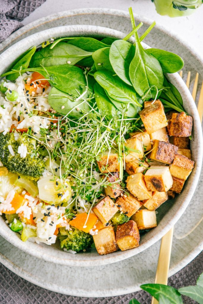 Nahaufnahme von Gemüsereis mit gebratenem Tofu aus der Vogelperspektive. Bowl auf der linken Seite angeschnitten.
