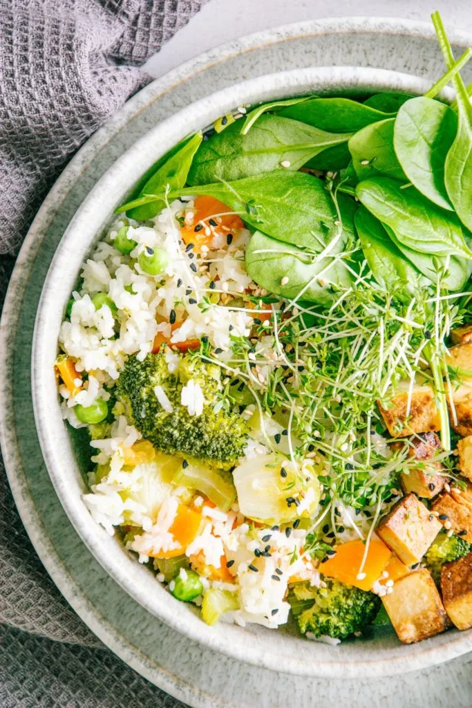 Nahaufnahme von Gemüsereis mit gebratenem Tofu aus der Vogelperspektive. Bowl auf der rechten Seite angeschnitten.