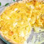Vegane Kürbis-Quiche in einer gläsernen runden Form im 45-Grad-Winkel fotografiert. Ein Viertel der Quiche wurde bereits aus der Form genommen.