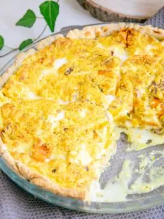 Vegane Kürbis-Quiche in einer gläsernen runden Form im 45-Grad-Winkel fotografiert. Ein Viertel der Quiche wurde bereits aus der Form genommen.