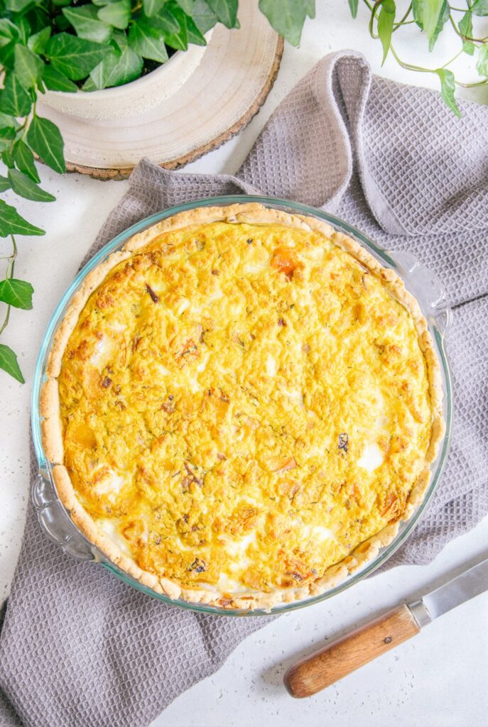 Vegane Kürbis-Quiche in einer runden Tarteform aus Glas aus der Vogelperspektive fotografiert.