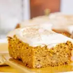 Ein Stück veganer zuckerfreier Kürbiskuchen fotografiert auf Augenhöhe, sodass die Vorderseite und eine Seite sichtbar sind. Detailaufnahme in orangen Herbstfarben.
