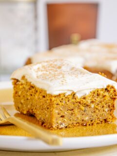 Ein Stück veganer zuckerfreier Kürbiskuchen fotografiert auf Augenhöhe, sodass die Vorderseite und eine Seite sichtbar sind. Detailaufnahme in orangen Herbstfarben.