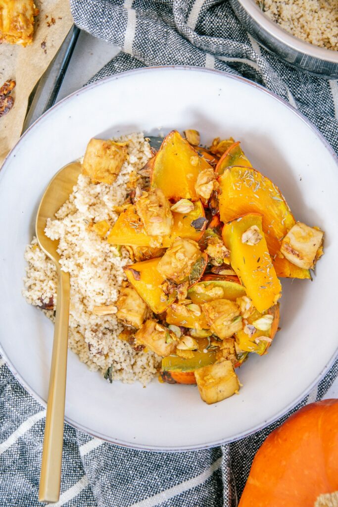 Ofen-Kürbis mit Knusper-Tofu und Couscous in einer graublauen Schüssel mit goldenem Löffel. Nahaufnahme von oben.