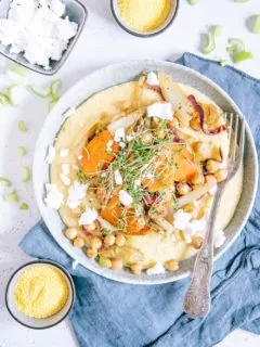 Schmorgemüse mit Cremepolenta, Kichererbsen, veganem Feta und Kresse auf einem grau-grünen Teller mit einer rustikalen Gabel aus der Vogelperspektive fotografiert.