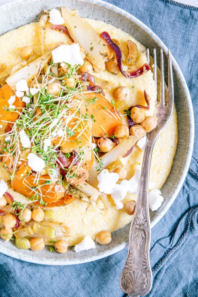 Nahaufnahme von Schmorgemüse mit Cremepolenta, Kichererbsen, veganem Feta und Kresse aus der Vogelperspektive. Teller von links angeschnitten.