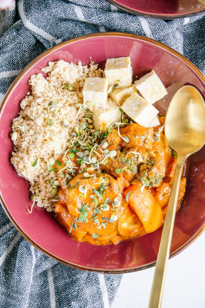 Nahaufnahme von schnellem Pfannengemüse mit würziger Sauce, Couscous und Tempeh mit goldenem Löffel aus der Vogelperspektive.