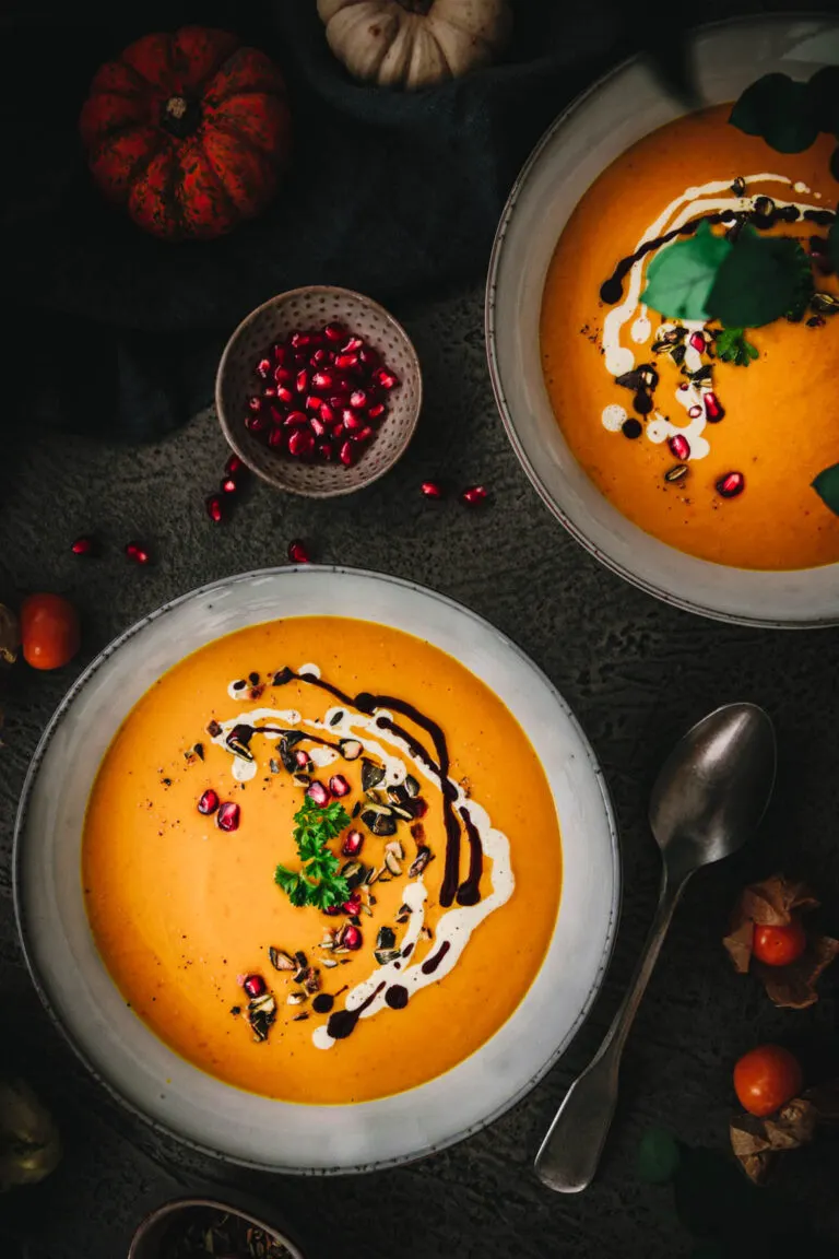 Zwei Teller Kürbissuppe garniert mit pflanzlicher Sahne, Kürbiskernöl, gerösteten Kürbiskernen, Petersilie und Granatapfelkernen
