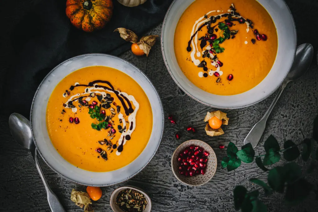 Zwei große Teller Kürbissuppe mit Löffeln von oben fotografiert