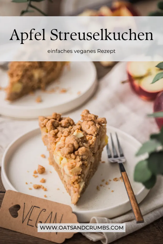 Ein Stück Apfel Streuselkuchen auf einem Teller cremeweißen Teller mit Kuchengabel und mit einem Anhänger mit der Aufschrift "vegan" davor