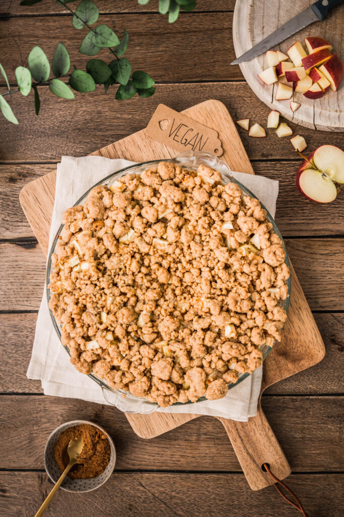 Veganer Apfel Streuselkuchen in einer runden Glasform auf einem Holzschneidebrett