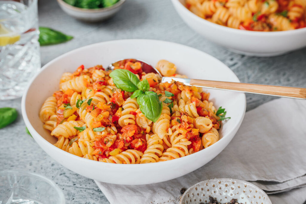 Ein Teller gesunde Pasta mit Gemüsesugo und frischem Basilikum