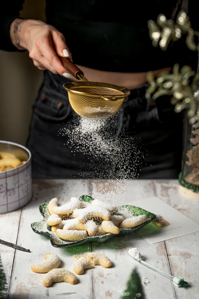 Staubzucker wird auf Vanillekipferl gesiebt.
