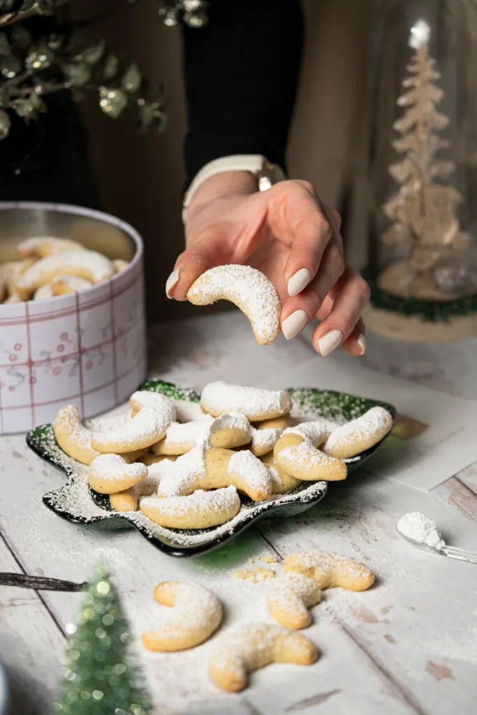 Hand nimmt ein Vanillekipferl vom Keksteller.