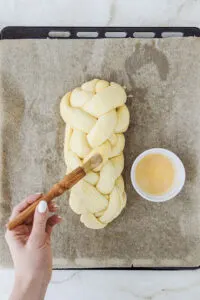 Geflochtener Brioche wird vor dem Backen bestrichen.