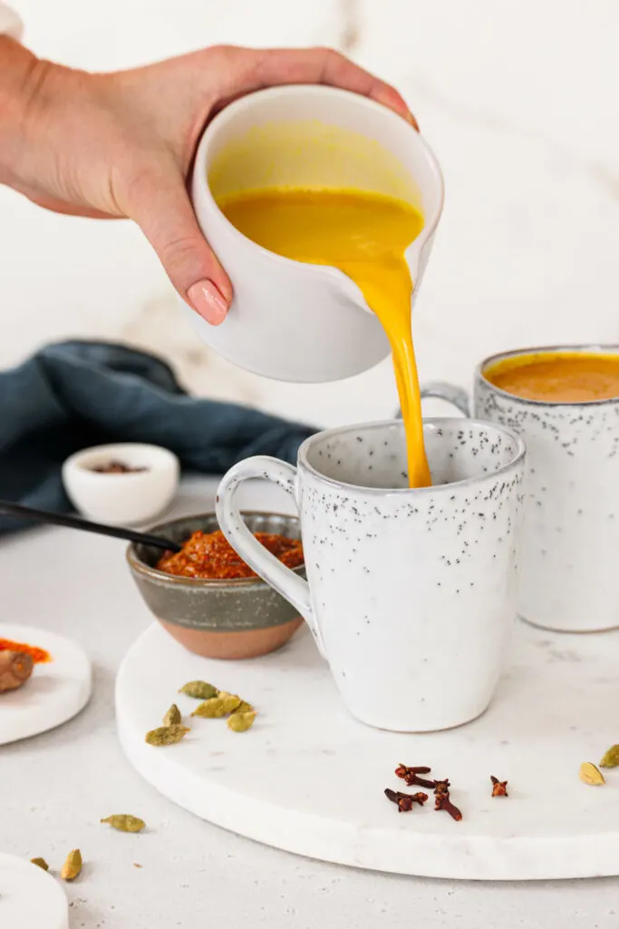 Goldene Milch wird aus einer Kanne in eine Tasse gegossen.