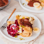 Haferflocken-Pfannkuchen mit Himbeer-Chia-Marmelade, Kokosjoghurt, Schoko-Mandelcreme, Bananenscheiben und gehackten Pistazien