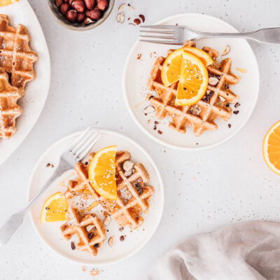 Vegane Vollkornwaffeln mit Orangenscheiben, gehackten Nüssen und Ahornsirup.