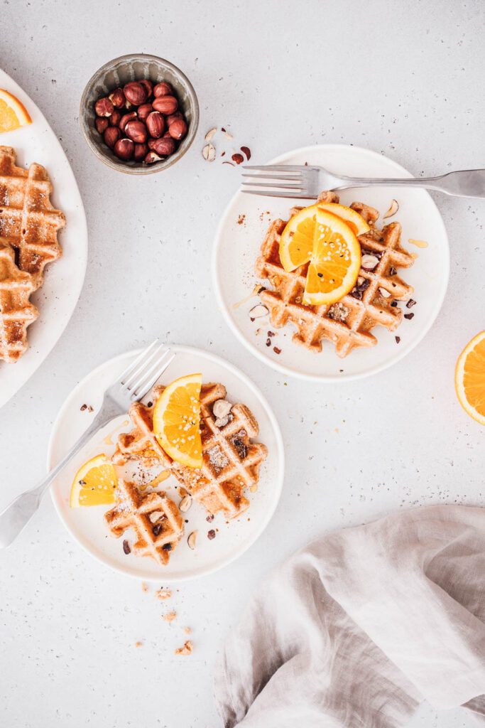 Vegane Vollkornwaffeln mit Orangenscheiben, gehackten Nüssen und Ahornsirup.