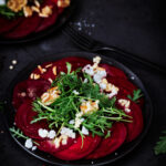 Rote Bete Carpaccio auf schwarzem Teller und schwarzem Untergrund.