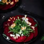 Rote Bete Carpaccio auf schwarzem Teller und schwarzem Untergrund.