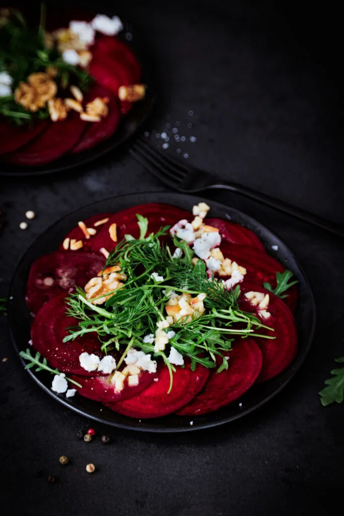 Rote Bete Carpaccio auf schwarzem Teller und schwarzem Untergrund.