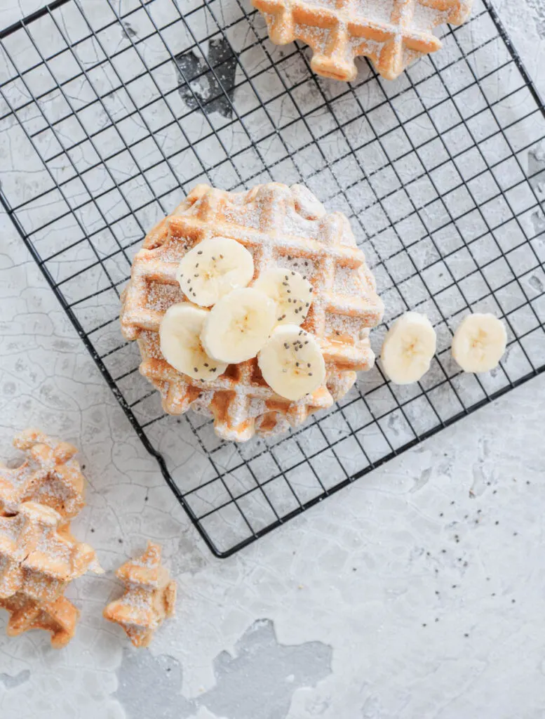 Bananenwaffeln mit Bananenscheiben und Chiasamen auf schwarzem Kuchengitter.