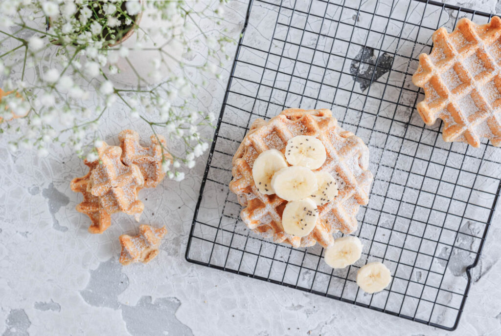 Schnelle Bananenwaffeln ohne Zucker auf hellem Untergrund mit weißem Schleierkraut im Bild.