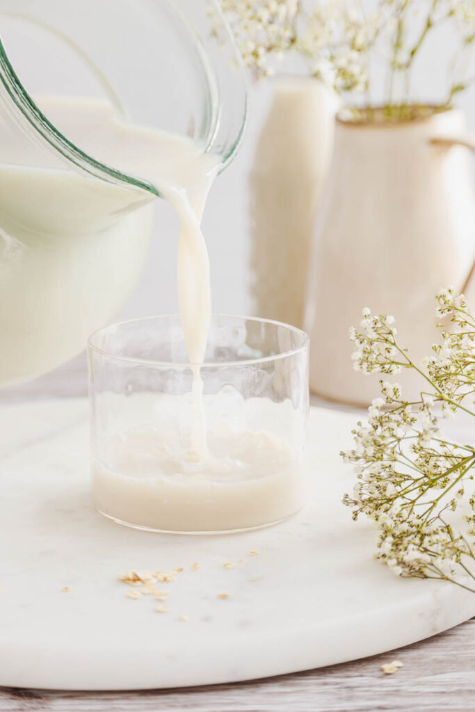 Selbstgemachte Hafermilch wird von einem Krug in ein Glas gegossen.