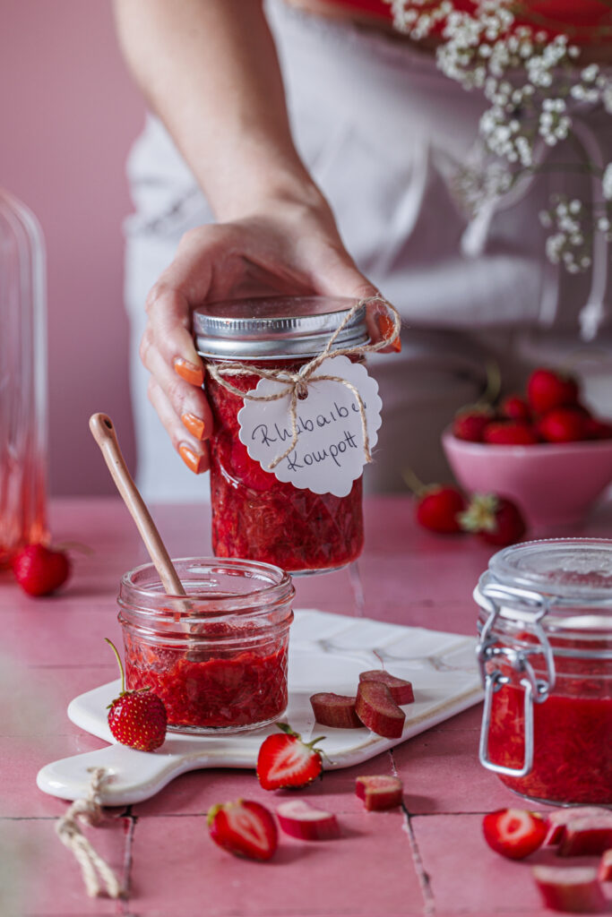 Hand hält ein Glas Rhabarberkompott mit selbst beschriftetem Anhänger.