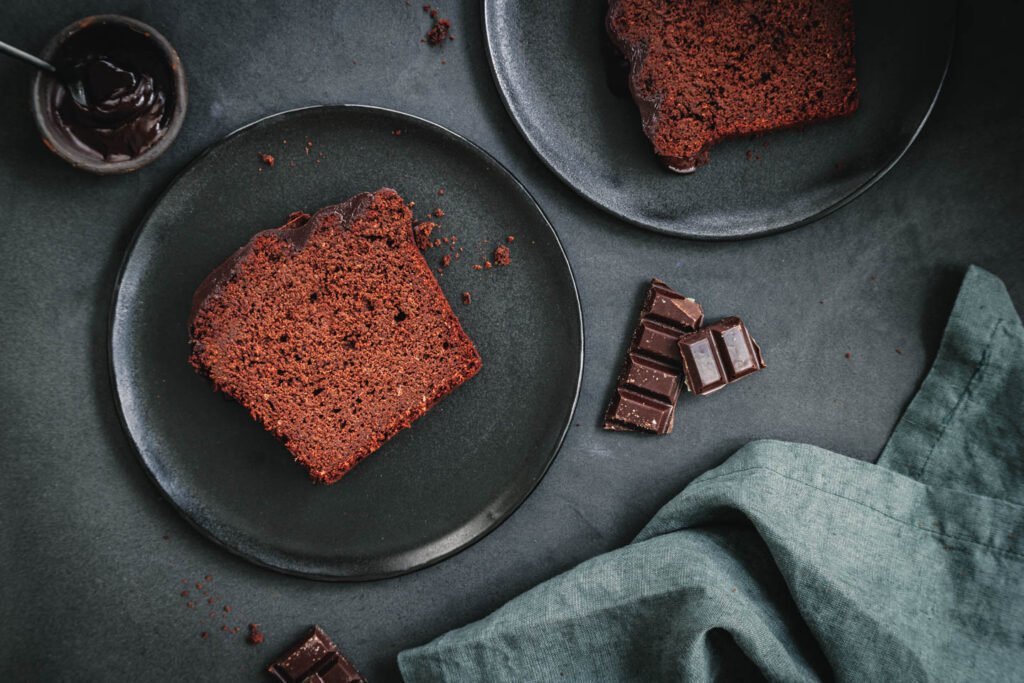 Ein Stück Schokokuchen ohne Zucker mit Schokoglasur auf schwarzem Teller.