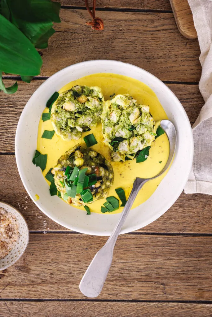 Vegane Bärlauchknödel mit cremiger Käsesauce in heller Schale mit rustikalem Löffel.