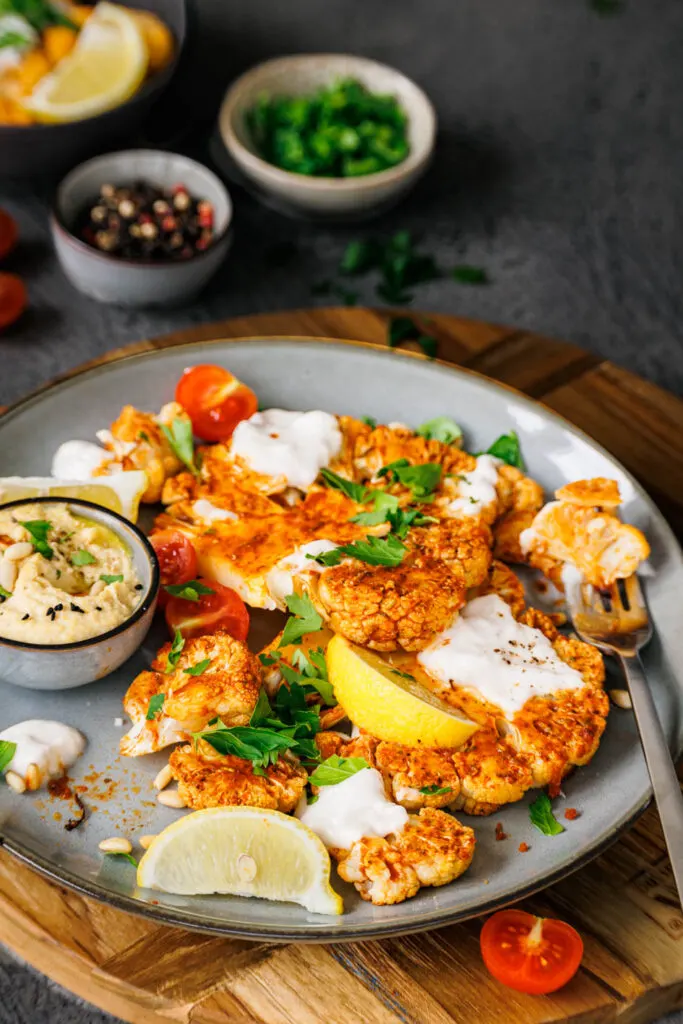 Köstliche Blumenkohl-Schnitzel garniert mit Kokosjoghurt, Cherrytomaten, Zitronenspalten, Pinienkernen und Petersilie.