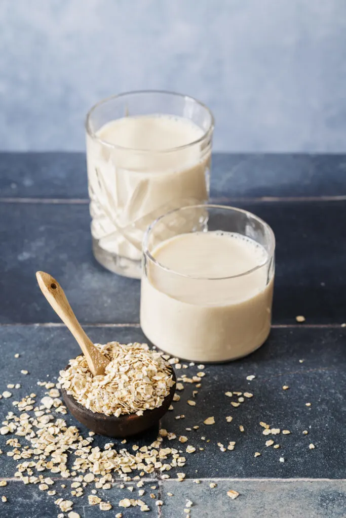 Zwei Gläser Hafermilch und eine kleine Schale mit zarten Haferflocken.