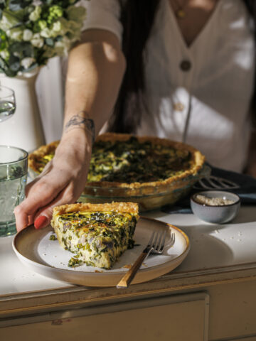 Hand nimmt einen Teller mit einem Stück Bärlauch-Quiche.