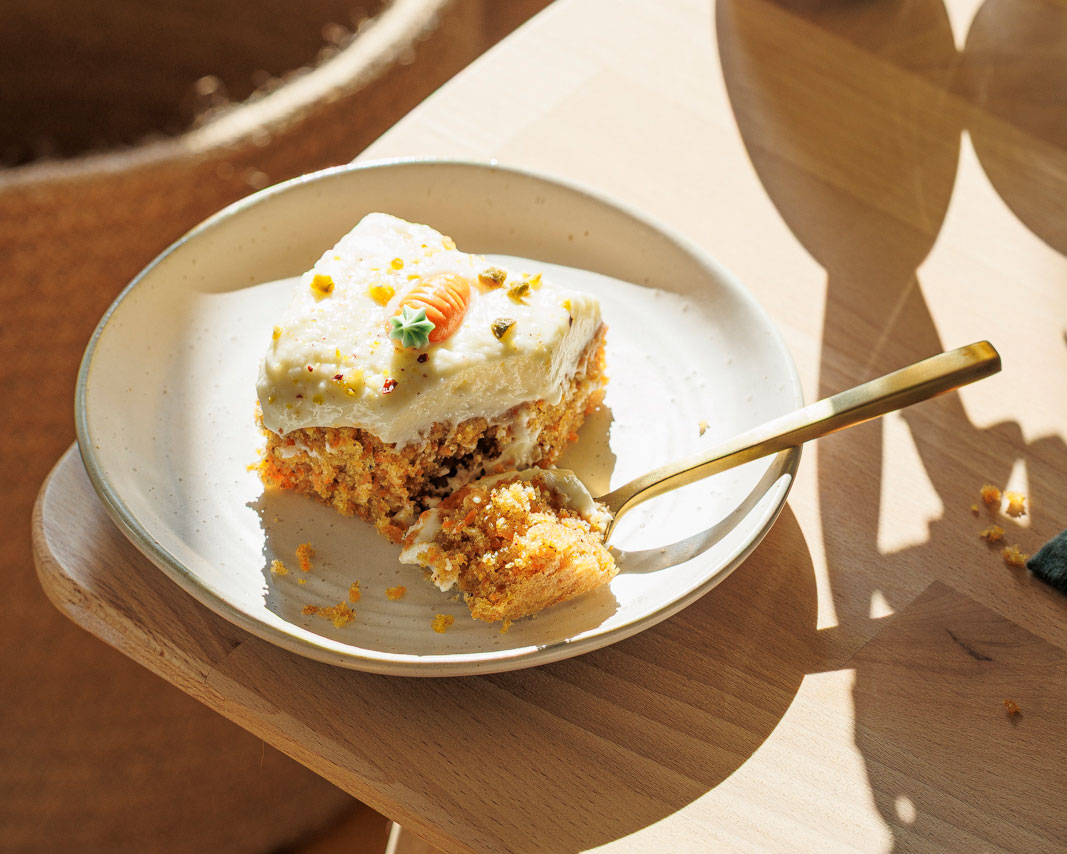 Ein Stück Karottenkuchen mit Frischkäsecreme auf Teller in der frühlingshaften Morgensonne.