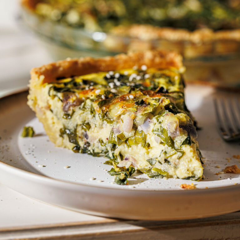 Nahaufnahme von einem Stück Frühlingshafte Bärlauch-Quiche mit Dinkel-Sesam-Mürbteig.