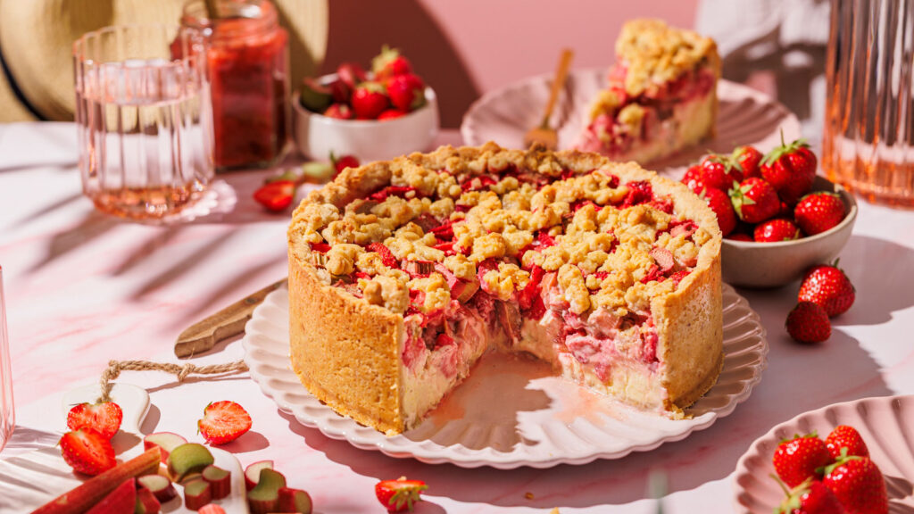 Anschnitt von saftigem Rhabarber-Streuselkuchen mit Erdbeeren und Quark.