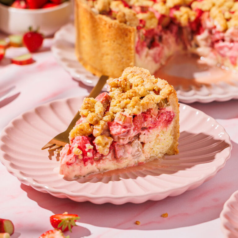 Nahaufnahme von einem Stück Erdbeer-Rhabarber-Streuselkuchen mit Quarkcreme.