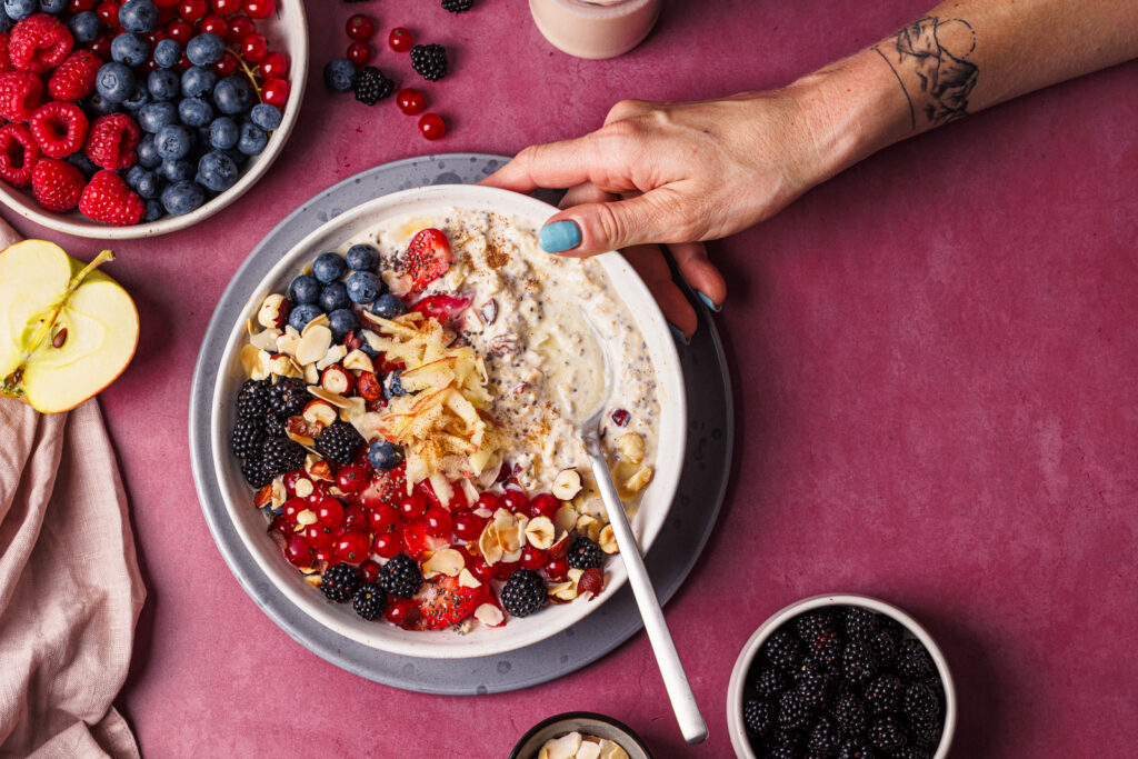 Hand an einer Schüssel mit proteinreichem Bircher Müsli – fotografiert aus der Vogelperspektive.